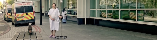 Heavily cropped still from Clinical Intervention  — Episode 19 of The MUTE Series. A pregnant woman on a drip is walking outside a hospital.